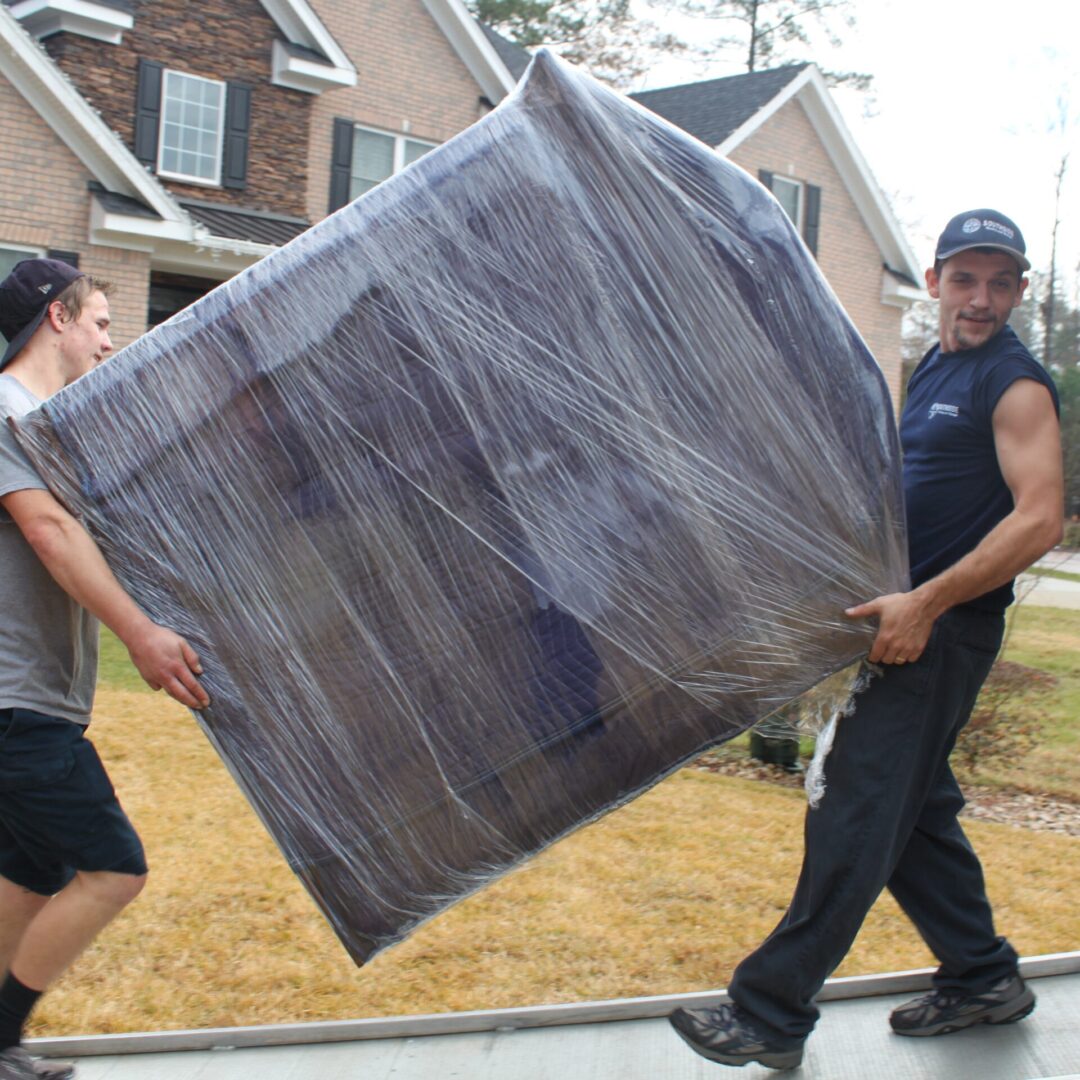 Two men moving a couch in front of a house.