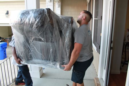 A man carrying a couch in a plastic bag.