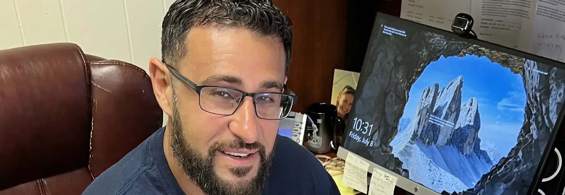 A man with glasses is sitting in front of a computer.