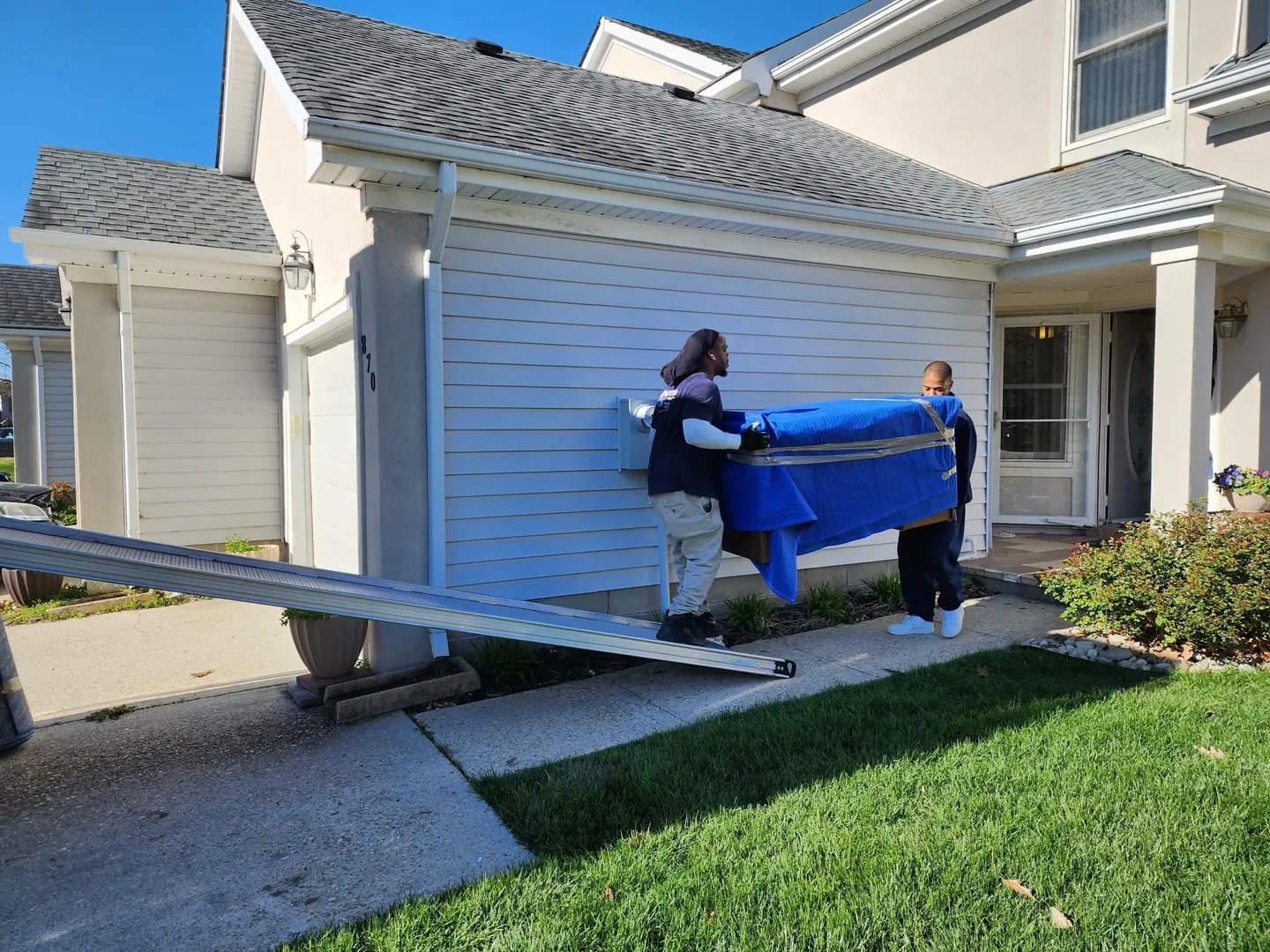 Two people moving a blue couch into the back of a house.