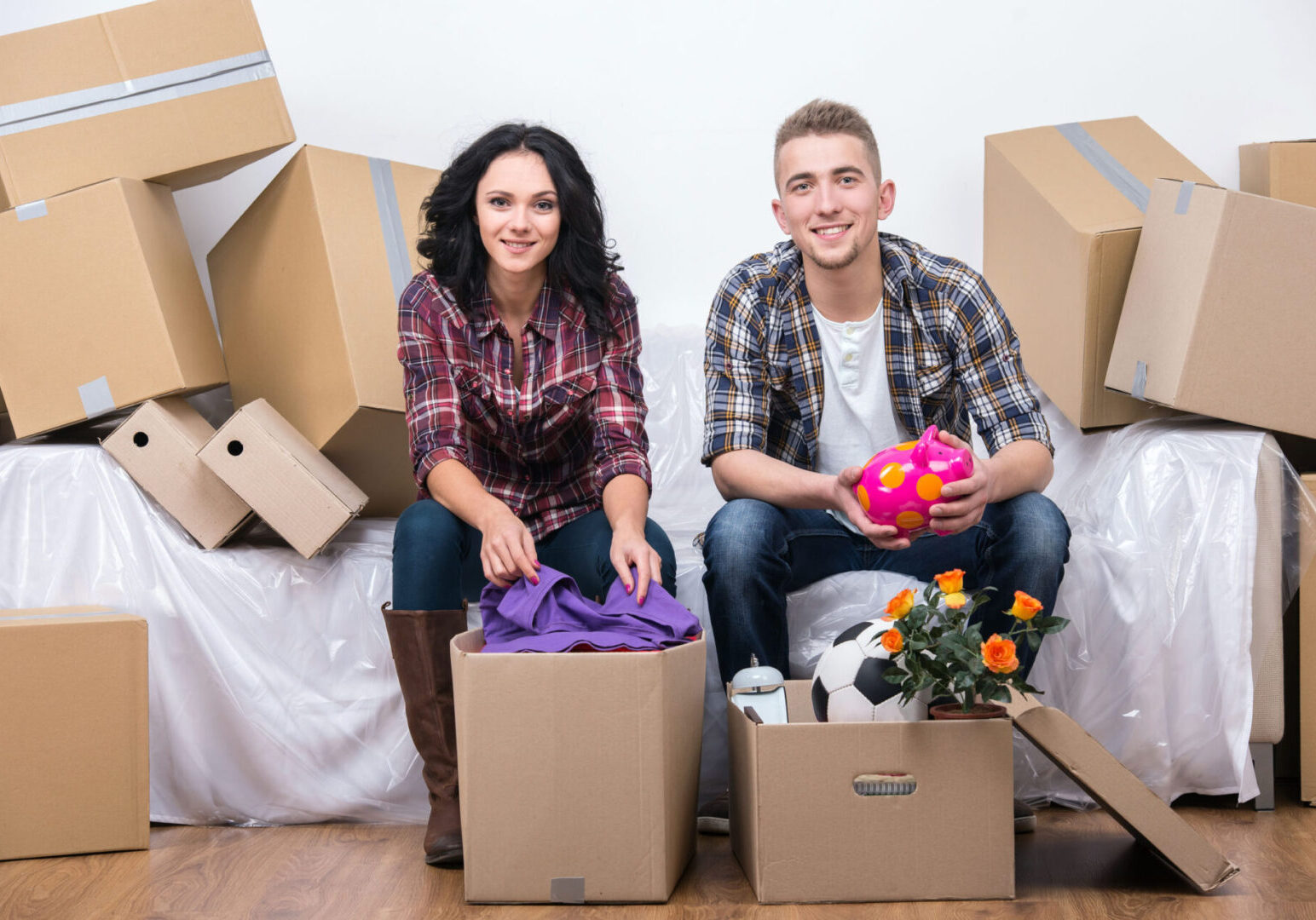A man and woman sitting on boxes in their new home.