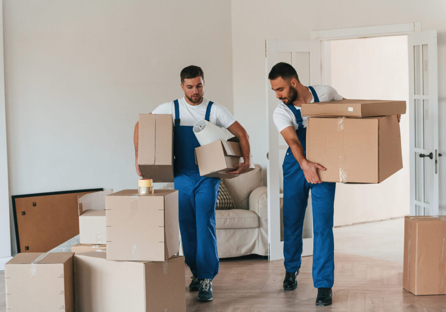 Front view, holding stuff. Two moving service employees in a room.